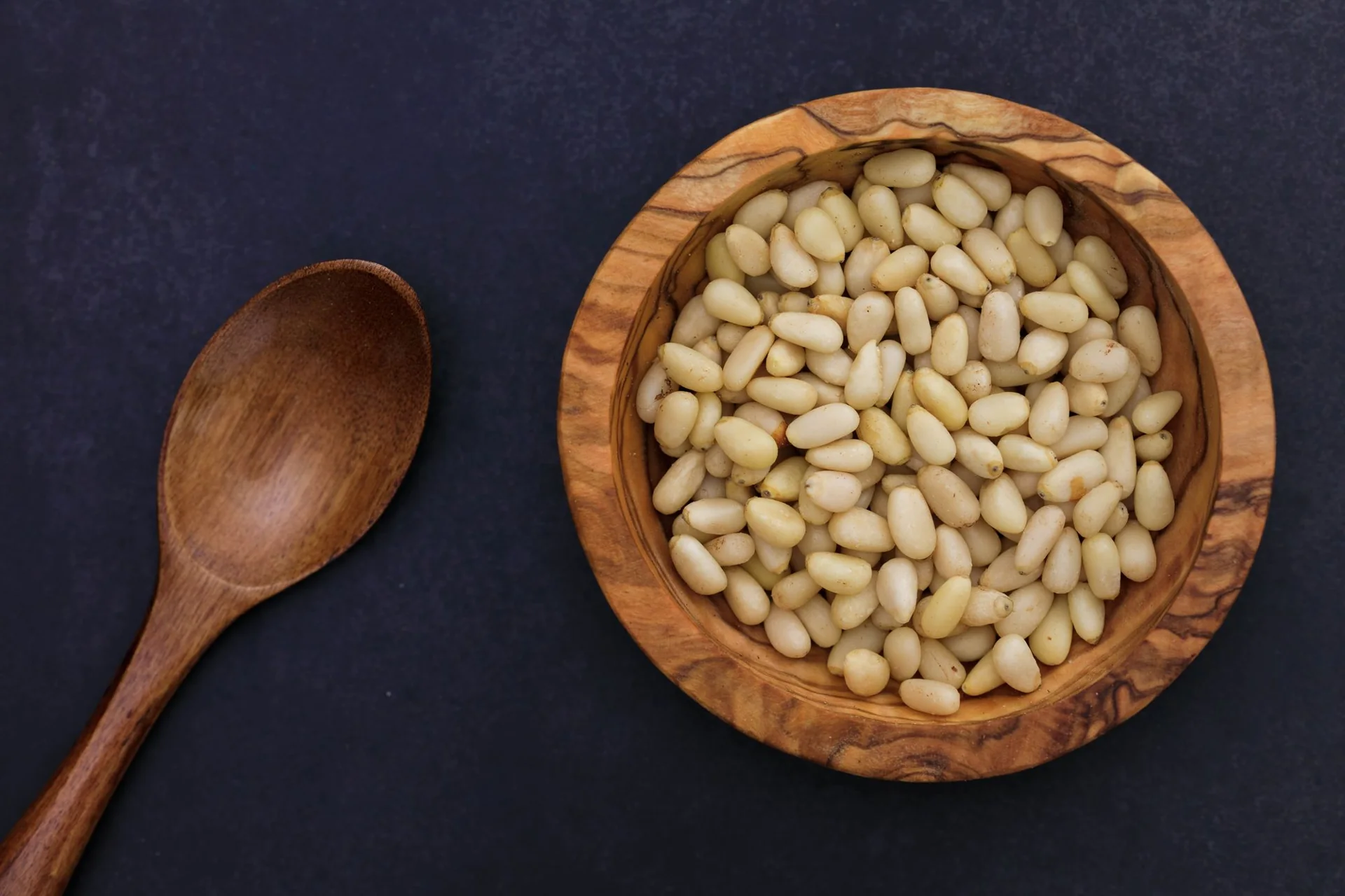 Pinienkerne in einer Holzschale mit Holzlöffel – Stimmungsbild, kein nachgewiesenes PINE-NUT-LATTE-Rezept