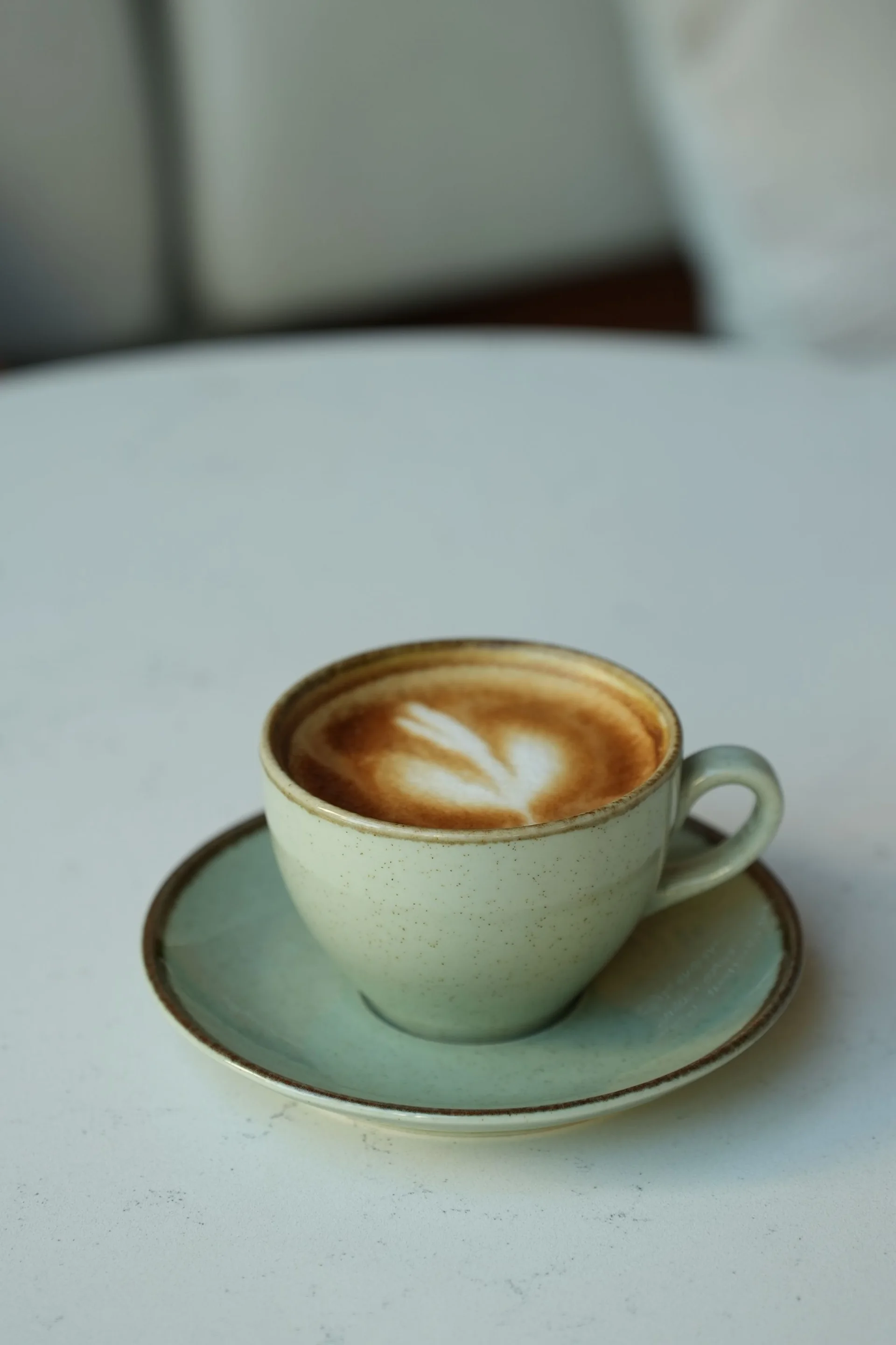 Cappuccino mit Latte Art auf einer Keramikuntertasse – Stimmungsbild, kein nachgewiesenes PINE-NUT-LATTE-Rezept